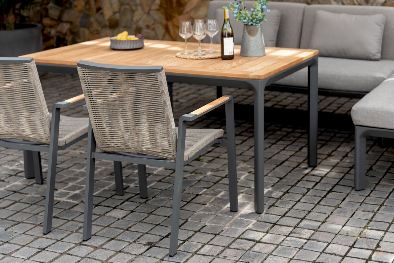Zwei moderne Stapelsessel aus Metall und Geflecht, seitliche Perspektive, an einem Holztisch im Freien aufgestellt.