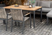 Twee moderne stapelstoelen van metaal en vlechtwerk, gezien vanaf de zijkant, opgesteld rond een houten tafel in de open lucht.