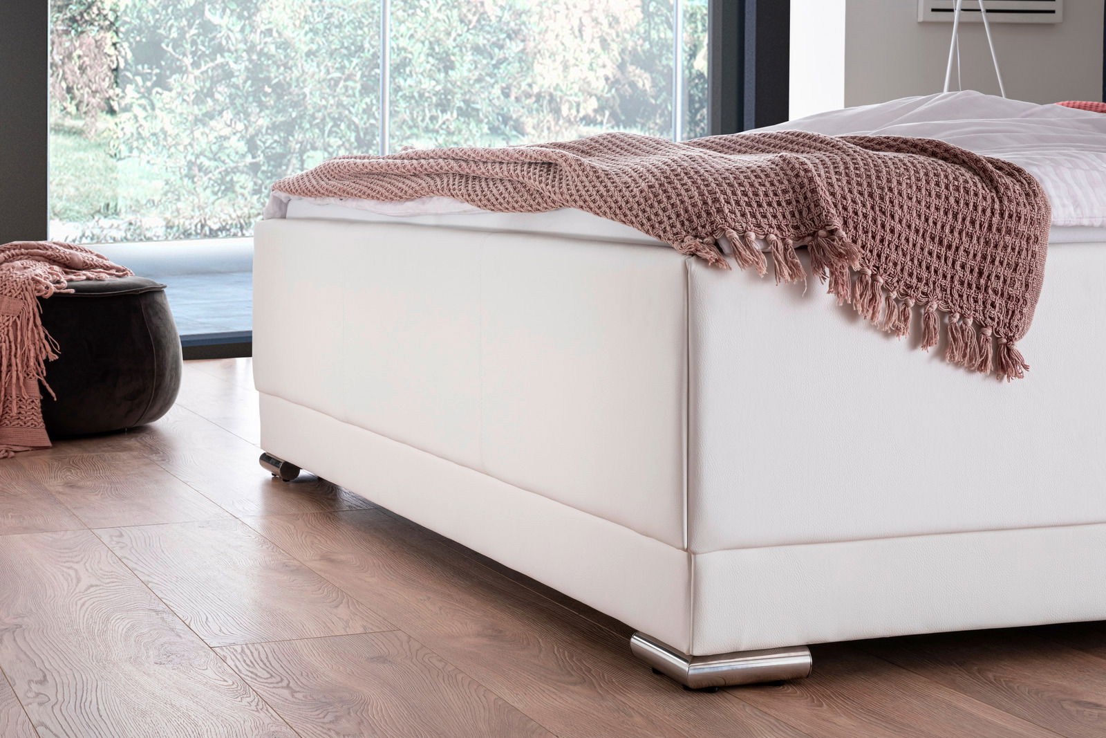 Nahaufnahme eines weißen Polsterbetts mit rosa Überwurf, seitliche Perspektive.