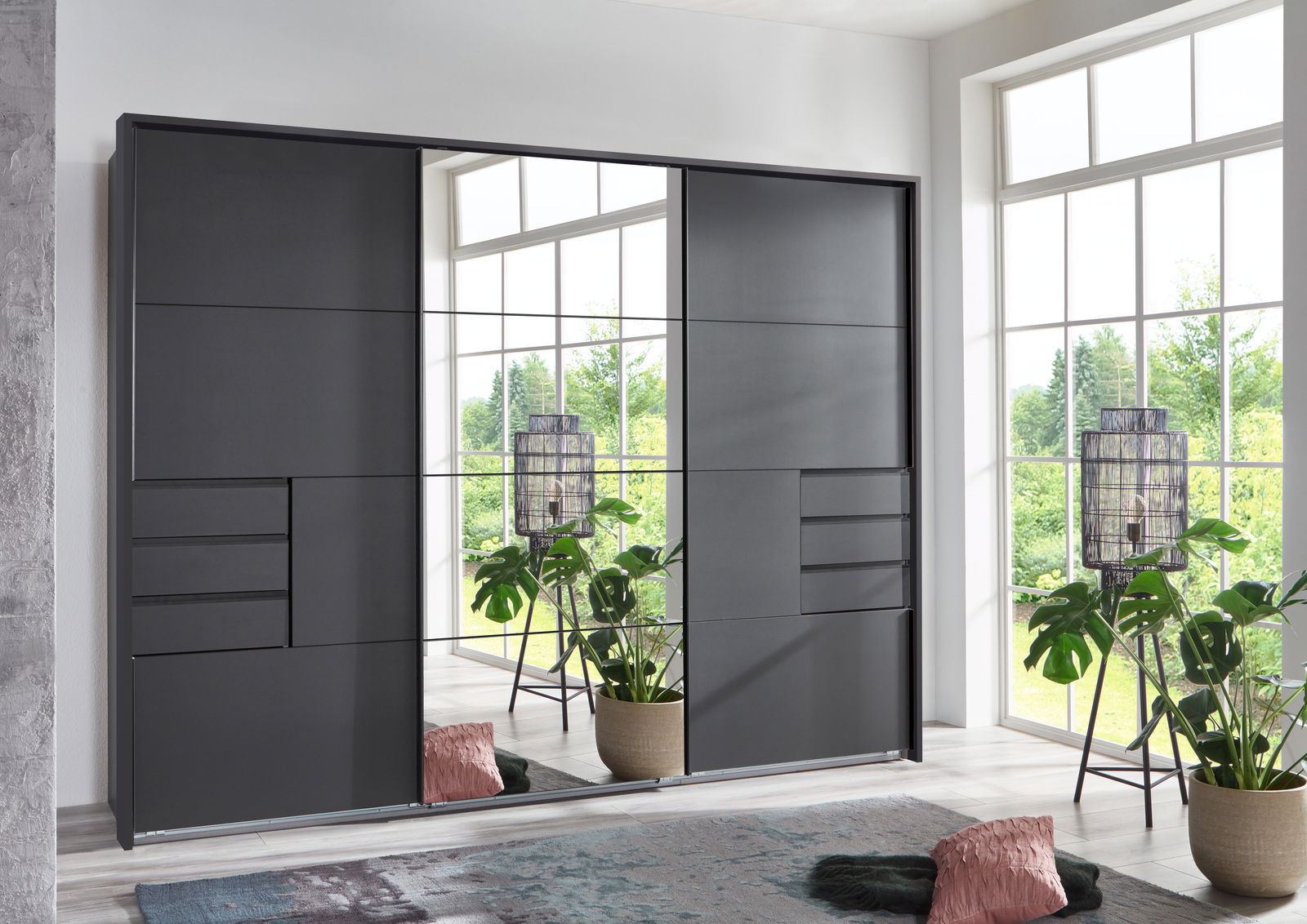 Z2 Schwebetürenschrank/Passp.3trg SAIGON Moderner Schwebetürenschrank in dunklem Design mit Spiegel in einem hellen Raum, seitliche Perspektive.