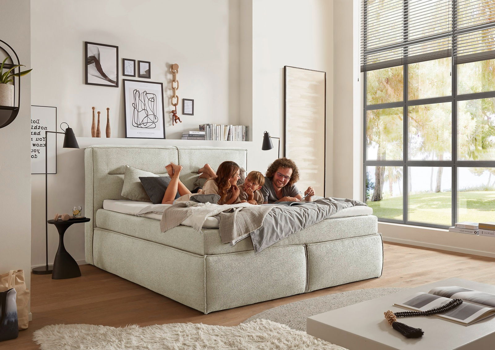Gemütliches Boxspringbett in einem modernen Schlafzimmer, seitliche Perspektive, mit einer Familie, die darauf entspannt.