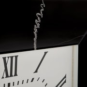 Nahaufnahme einer Wanduhr mit römischen Ziffern und einem schwarzen Rahmen, aus seitlicher Perspektive.