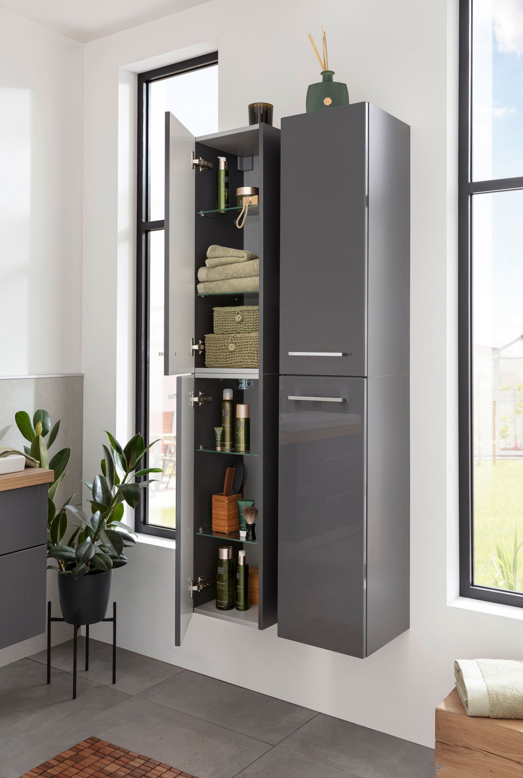 Moderner, grauer Hochschrank in einem Badezimmer, teilweise geöffnet, mit Handtüchern und Pflegeprodukten gefüllt. Perspektive von vorne.