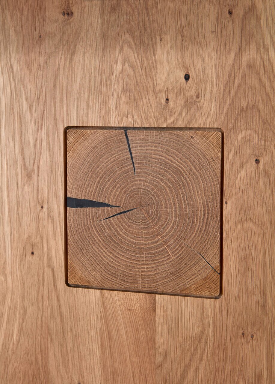 Close-up van een houten salontafel met zichtbare houtnerf en een vierkant inzetstuk van een dwarsdoorsnede van een boomstam in het midden, gezien van bovenaf.