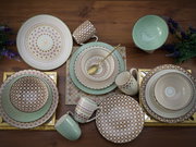 Kombiservice 16-tlg mit dekorativen Mustern in Grün- und Beigetönen, von oben fotografiert auf einem Holztisch arrangiert.