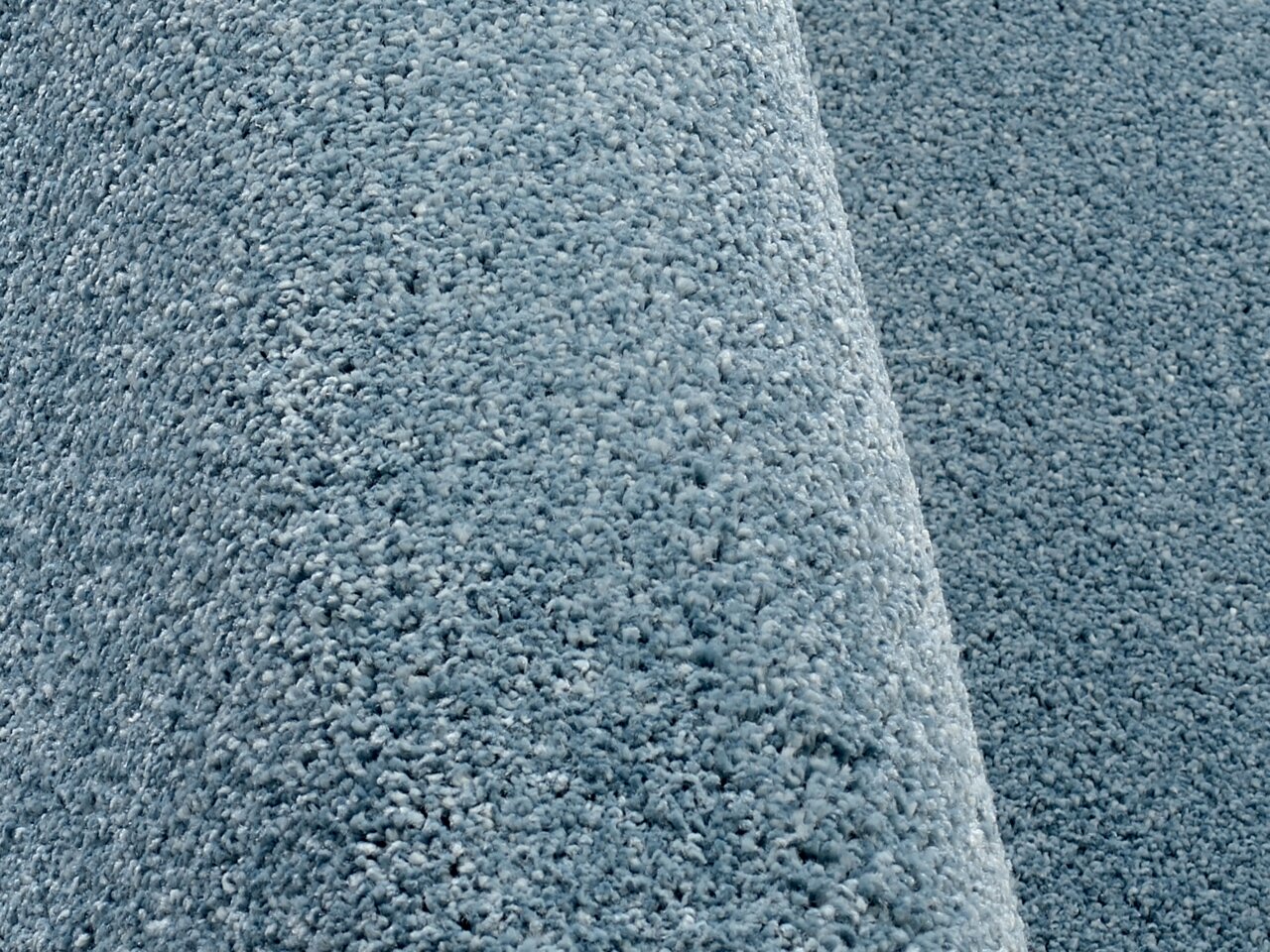 Nahaufnahme eines blauen Uni-Teppichs mit weicher, flauschiger Textur, seitliche Perspektive