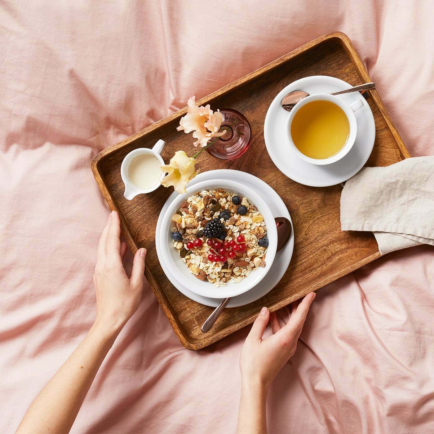Frühstückstablett mit einer Schale Müsli, einer Tasse Tee und einer kleinen Milchkanne, von oben fotografiert.