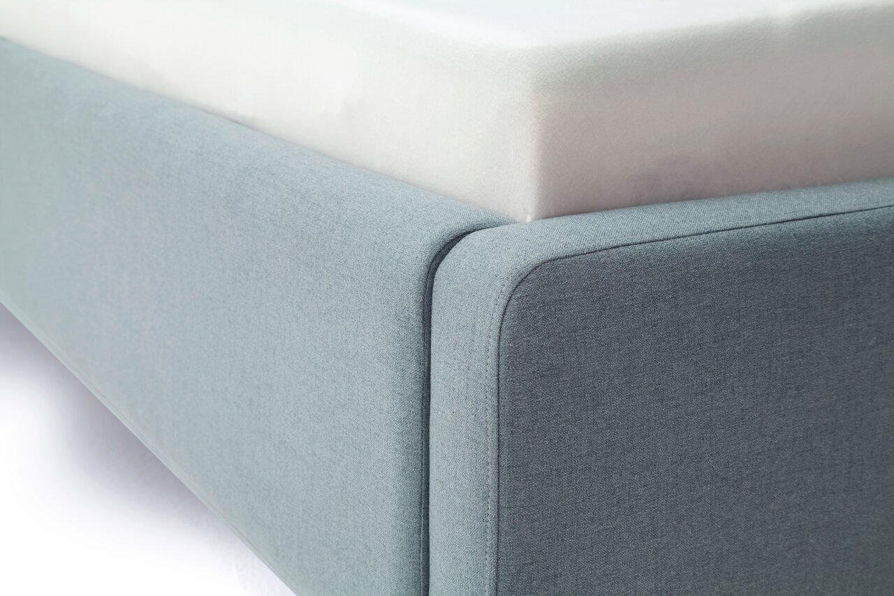 Nahaufnahme eines blauen Polsterbetts von der Seite, das die Ecke des Bettrahmens zeigt.