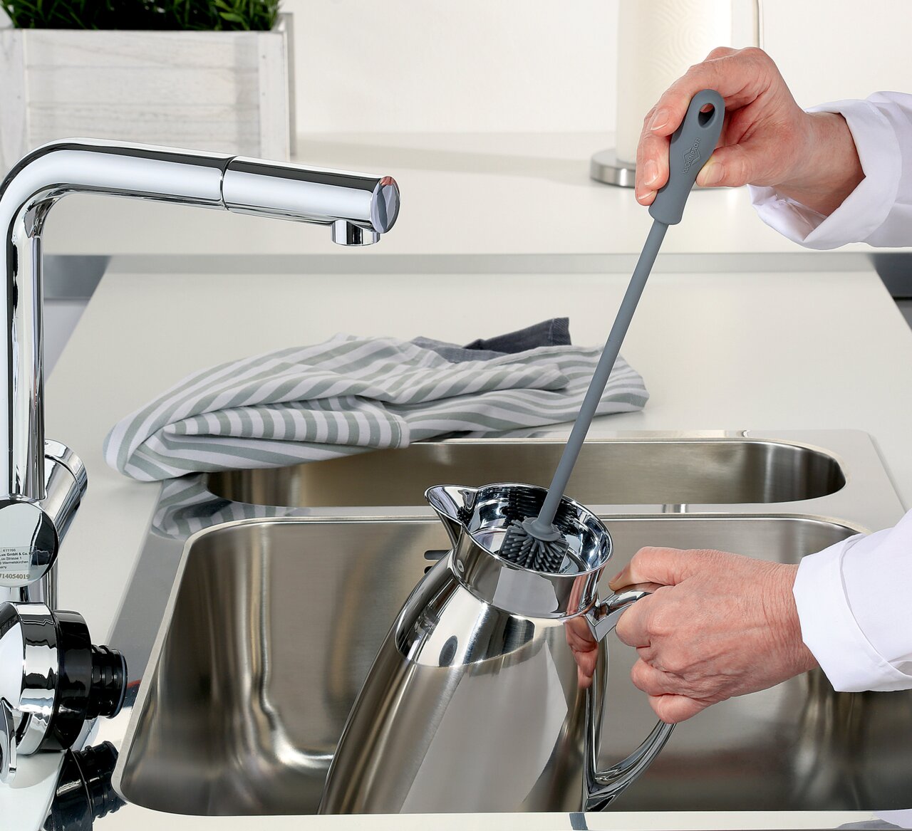 KÜCHENPROFI Spülbürste Graue Spülbürste in der Hand, die eine Kanne in einem modernen Küchenwaschbecken reinigt, seitliche Perspektive.