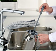 Graue Spülbürste in der Hand, die eine Kanne in einem modernen Küchenwaschbecken reinigt, seitliche Perspektive.