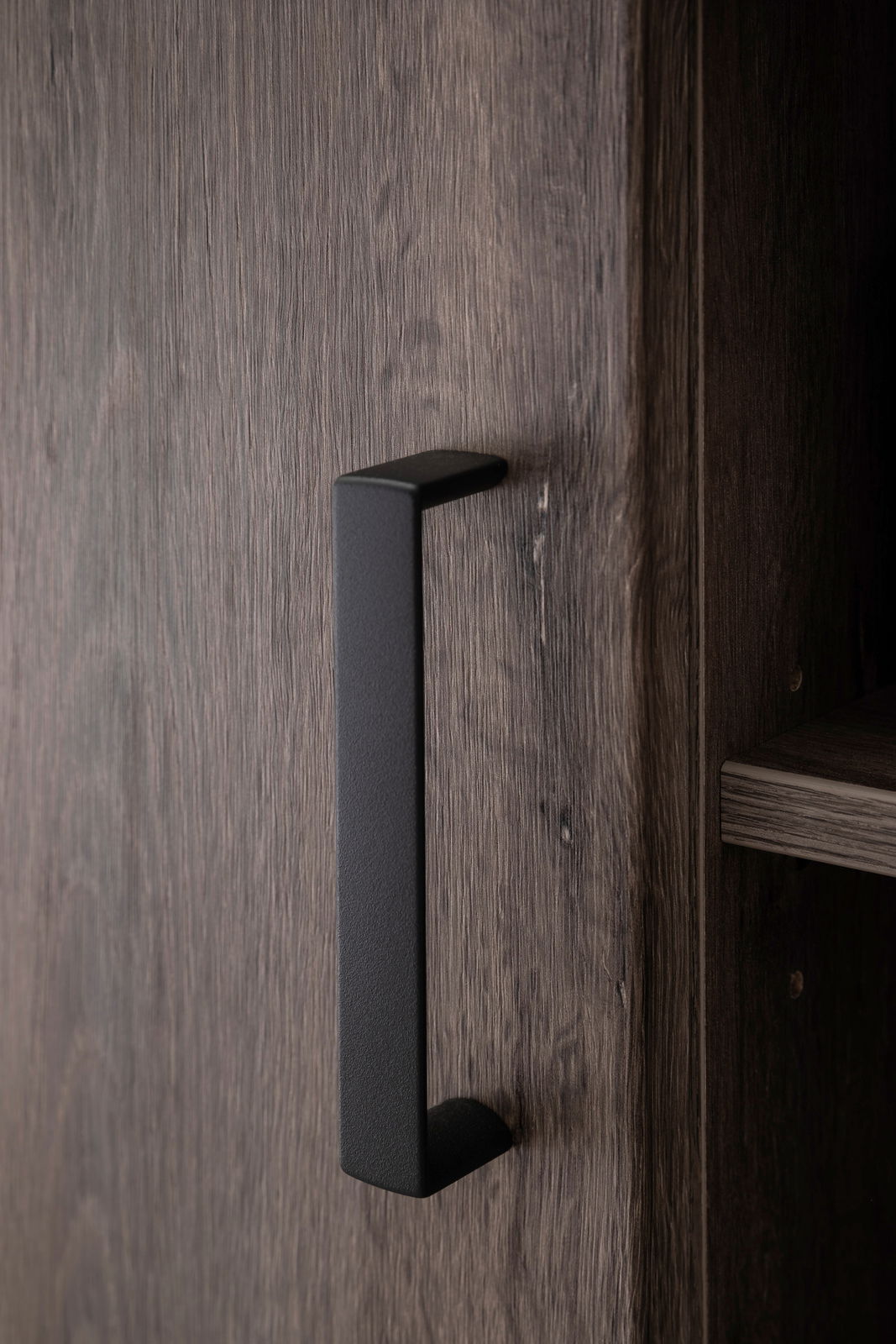 Nahaufnahme eines schwarzen Griffs an einer Holztür eines Sideboards, seitliche Perspektive