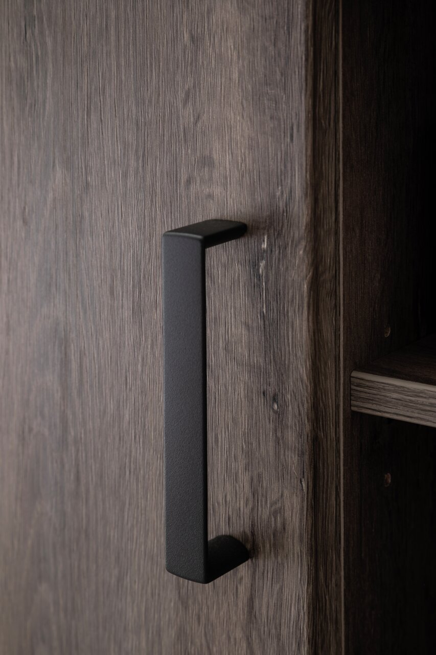Nahaufnahme eines schwarzen Griffs an einer Holztür eines Sideboards, seitliche Perspektive