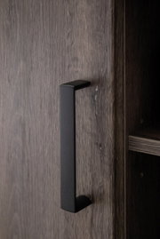 Nahaufnahme eines schwarzen Griffs an einer Holztür eines Sideboards, seitliche Perspektive