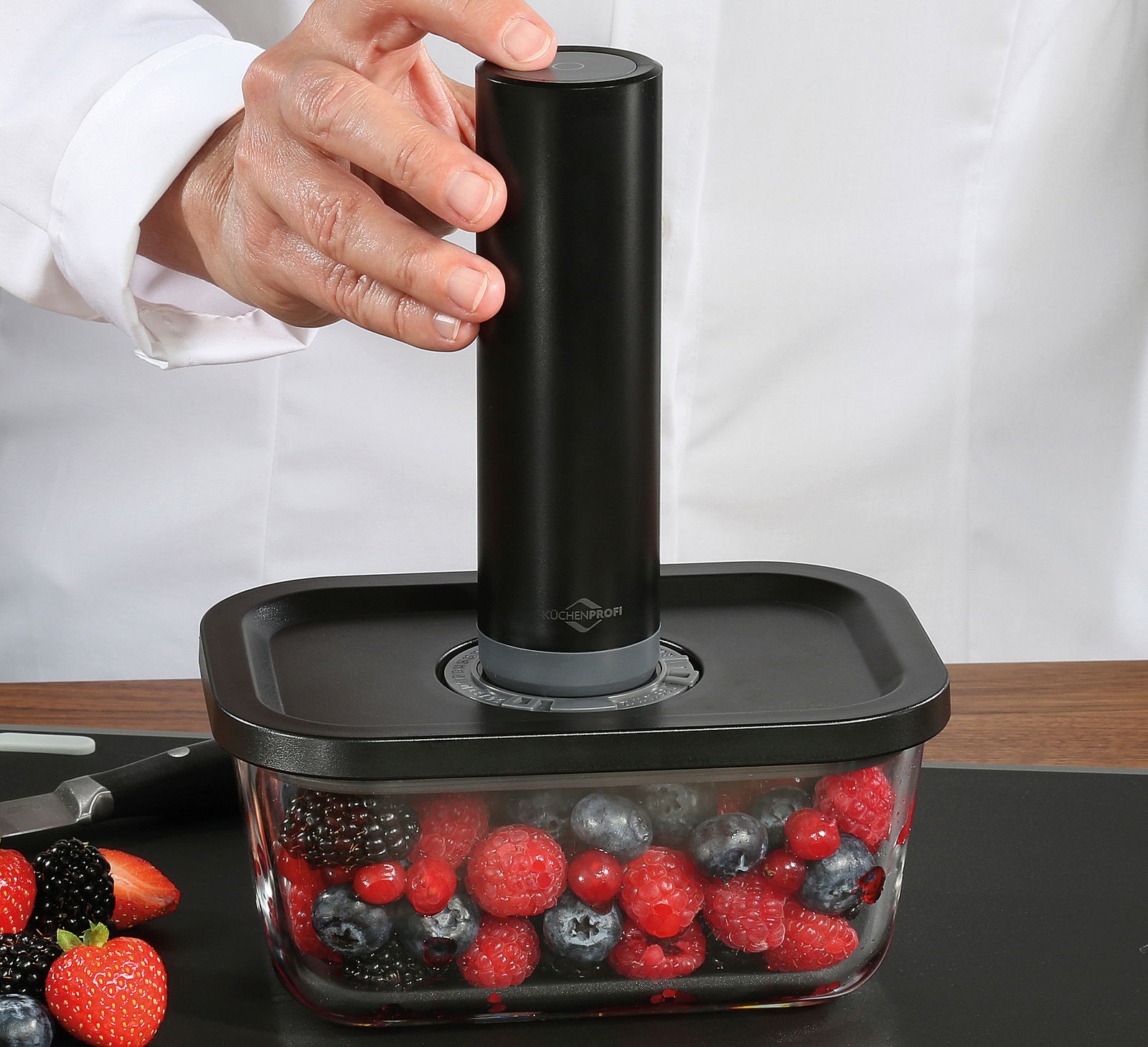 Vakuumier-Set EASYFRESH in seitlicher Perspektive, mit Hand, die das Gerät auf einem Behälter mit Beeren bedient.