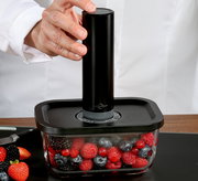 Vakuumier-Set EASYFRESH in seitlicher Perspektive, mit Hand, die das Gerät auf einem Behälter mit Beeren bedient.