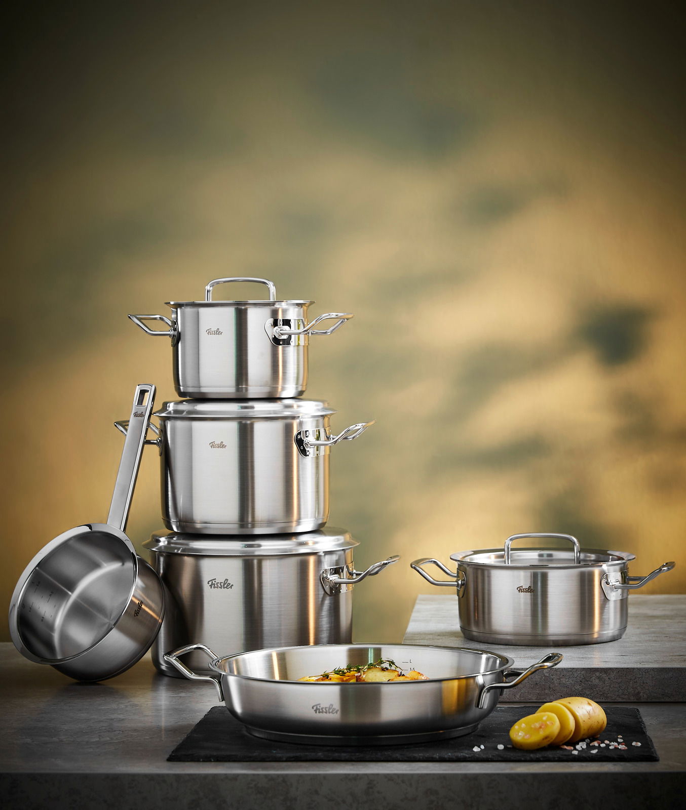 Fissler Topfset 5-tlg. inkl. Servierpfanne 28cm ORIGINAL PROFI COLLECTION Topfset Original-Profi 5-tlg. aus Edelstahl, bestehend aus mehreren Töpfen und Pfannen, auf einer Küchenarbeitsplatte präsentiert. Perspektive: seitlich von vorne.