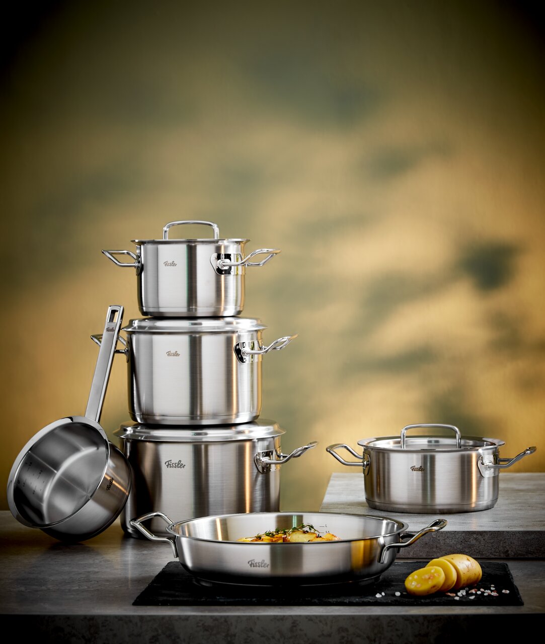 Fissler Topfset 5-tlg. inkl. Servierpfanne 28cm ORIGINAL PROFI COLLECTION Topfset Original-Profi 5-tlg. aus Edelstahl, bestehend aus mehreren Töpfen und Pfannen, auf einer Küchenarbeitsplatte präsentiert. Perspektive: seitlich von vorne.