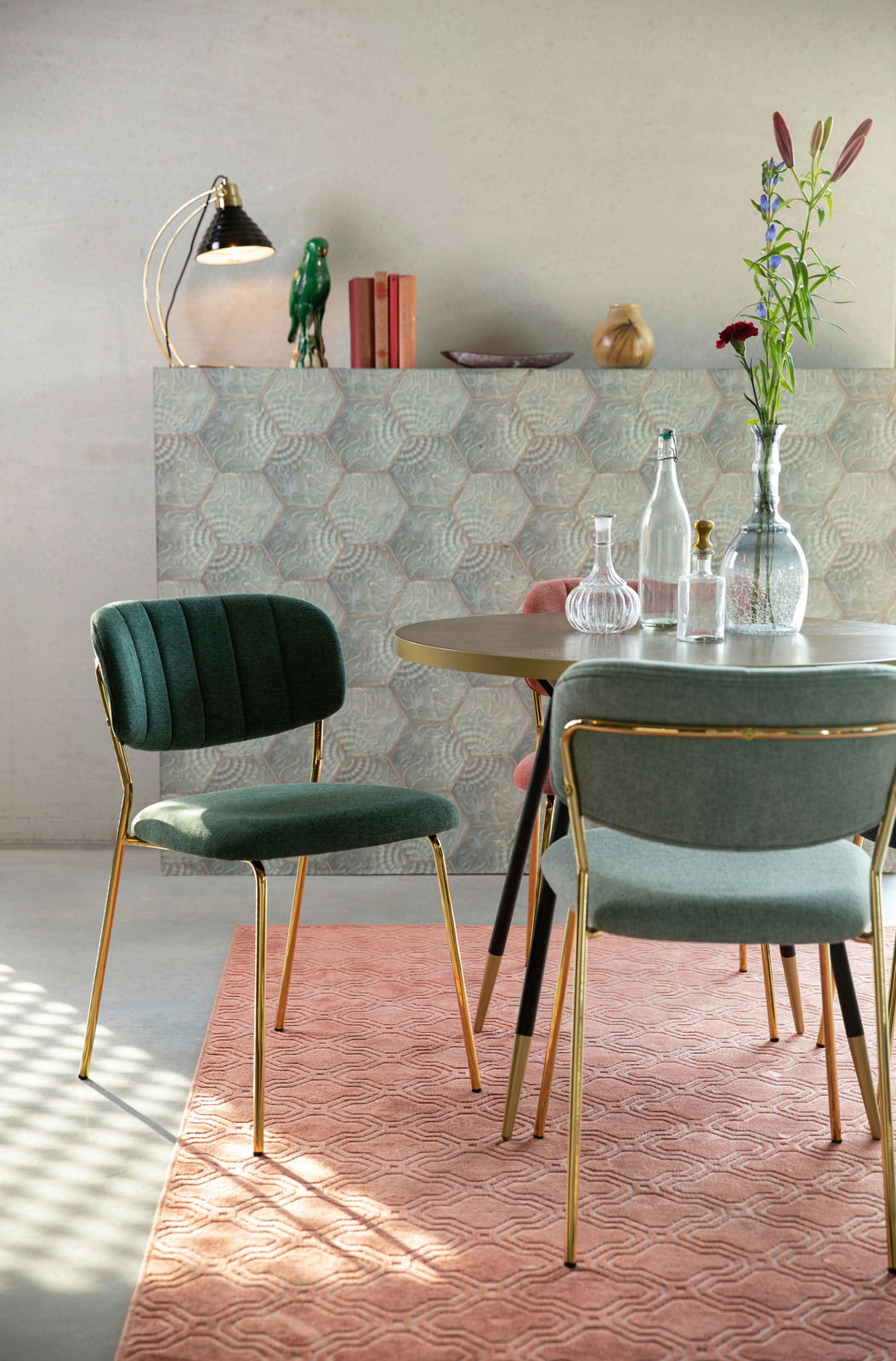 Grüner Stuhl mit goldenen Beinen, seitliche Perspektive, in einem stilvoll eingerichteten Raum mit Tisch und Dekoration.