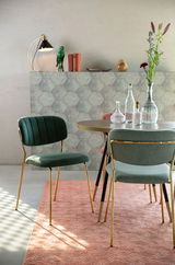Grüner Stuhl mit goldenen Beinen, seitliche Perspektive, in einem stilvoll eingerichteten Raum mit Tisch und Dekoration.
