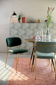 Groene stoel met gouden poten, gezien vanuit de zijkant, in een stijlvol ingerichte kamer met een tafel en decoratie.