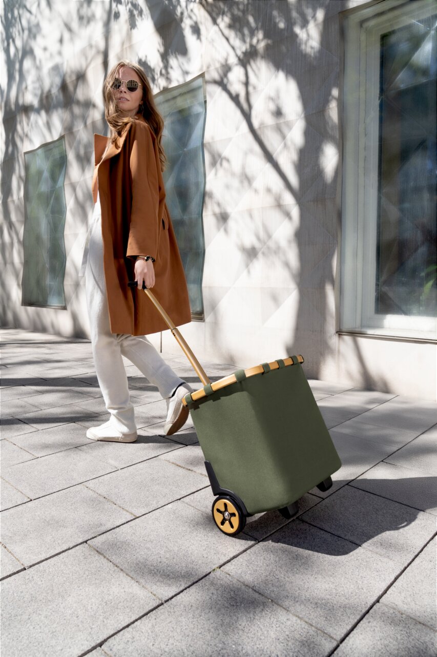 Frau zieht einen grünen carrycruiser auf einem Gehweg, seitliche Perspektive