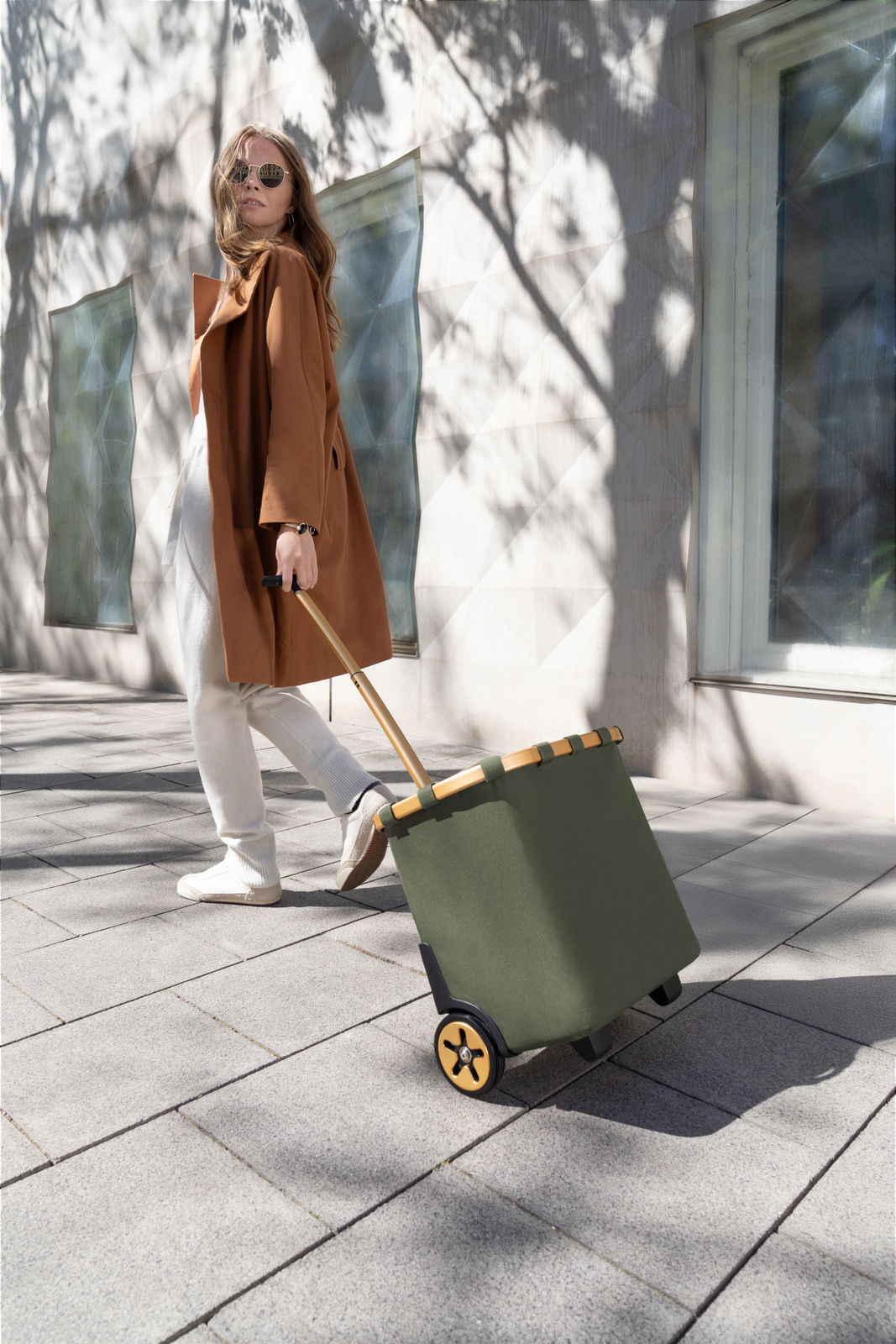 Frau zieht einen grünen carrycruiser auf einem Gehweg, seitliche Perspektive