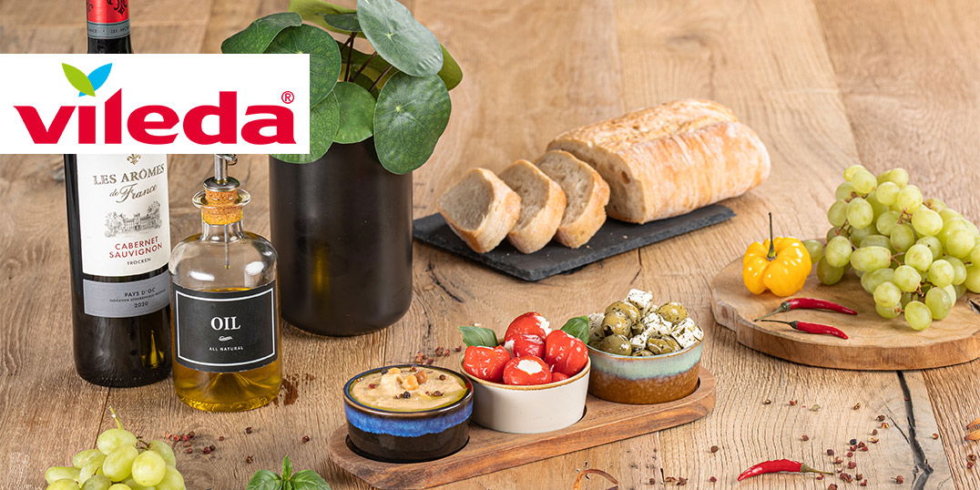 Ein rustikaler Holztisch mit Brot, Wein, Oliven, Käse, Trauben und Gewürzen, dekorativ angerichtet.