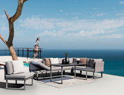 Moderne Outdoor-Sitzgruppe mit grauen Sofas und Tisch auf einer Terrasse mit Meerblick, seitliche Perspektive.