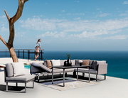 Moderne Outdoor-Sitzgruppe mit grauen Sofas und Tisch auf einer Terrasse mit Meerblick, seitliche Perspektive.