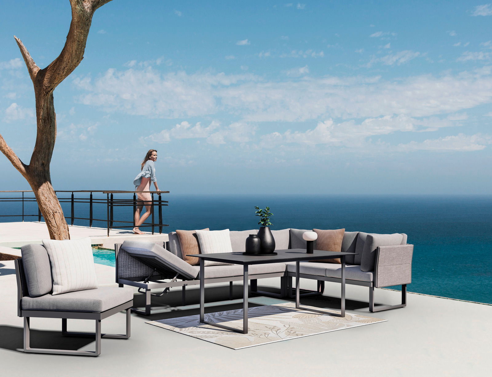Moderne Outdoor-Sitzgruppe mit grauen Sofas und Tisch auf einer Terrasse mit Meerblick, seitliche Perspektive.