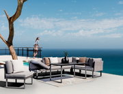 Moderne Outdoor-Sitzgruppe mit grauen Sofas und Tisch auf einer Terrasse mit Meerblick, seitliche Perspektive.