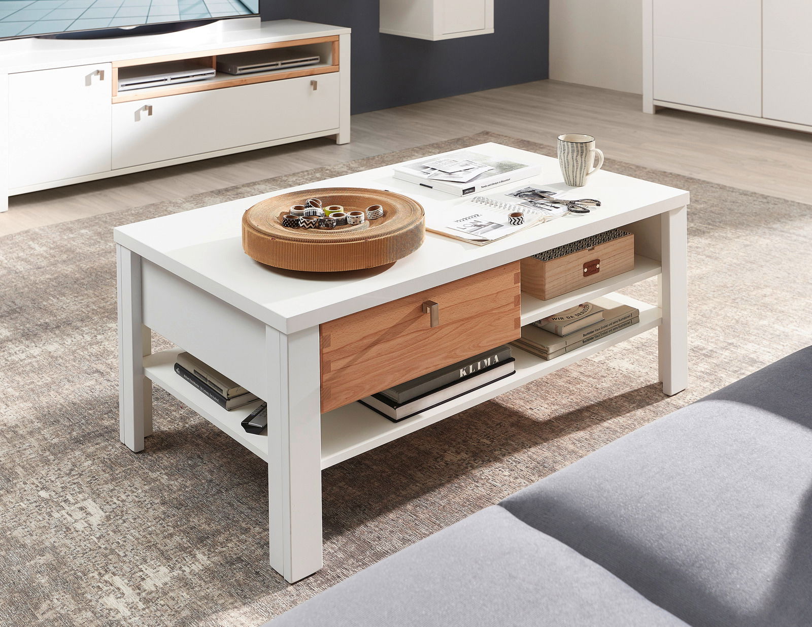 Moderner Couchtisch in Weiß mit Holzschublade, dekoriert mit einer Schale und Zeitschriften, seitliche Perspektive