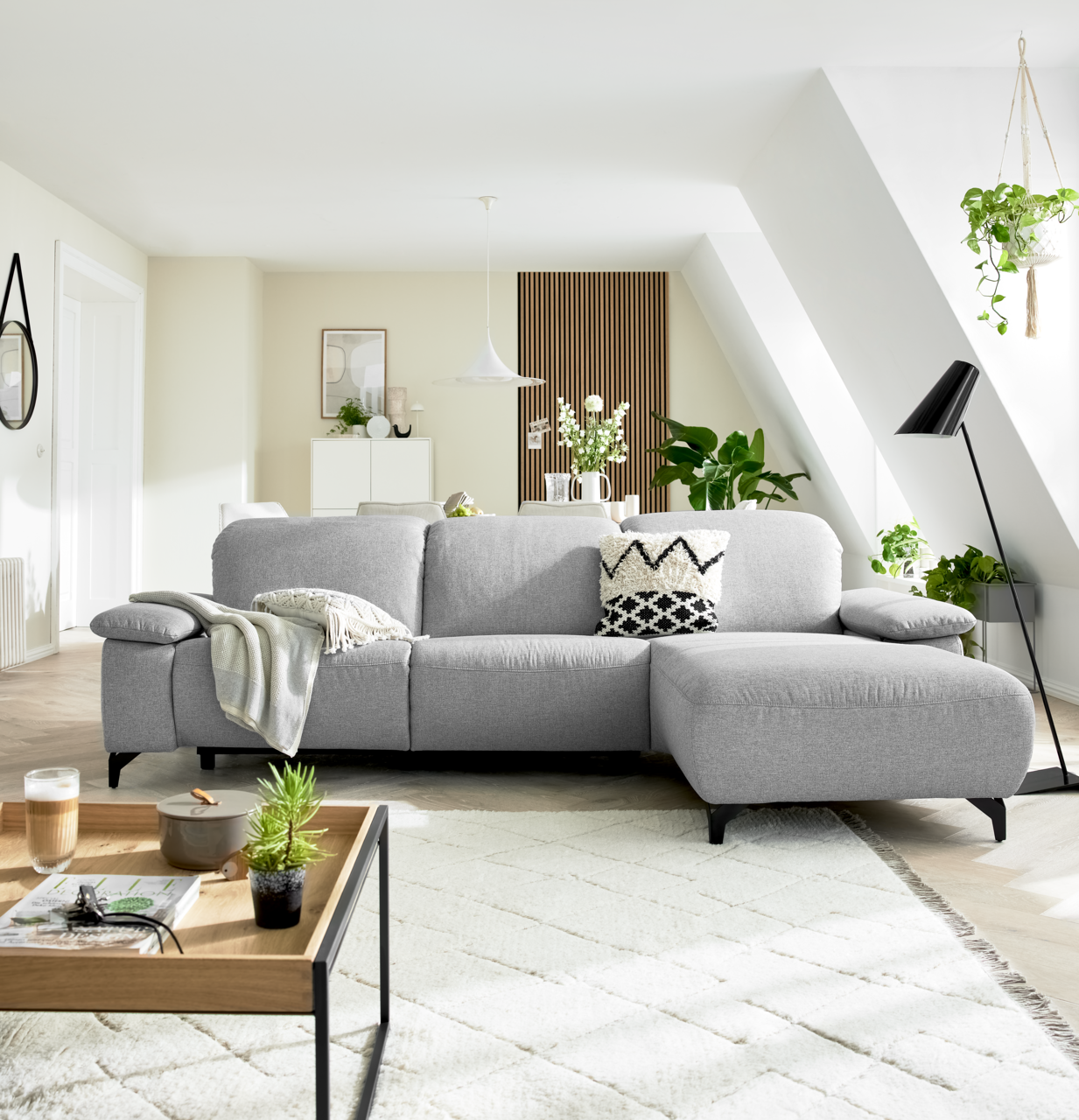 Graue Longchairkombination in einem modernen Wohnzimmer, frontal von vorne fotografiert, mit dekorativen Kissen und Pflanzen im Hintergrund.