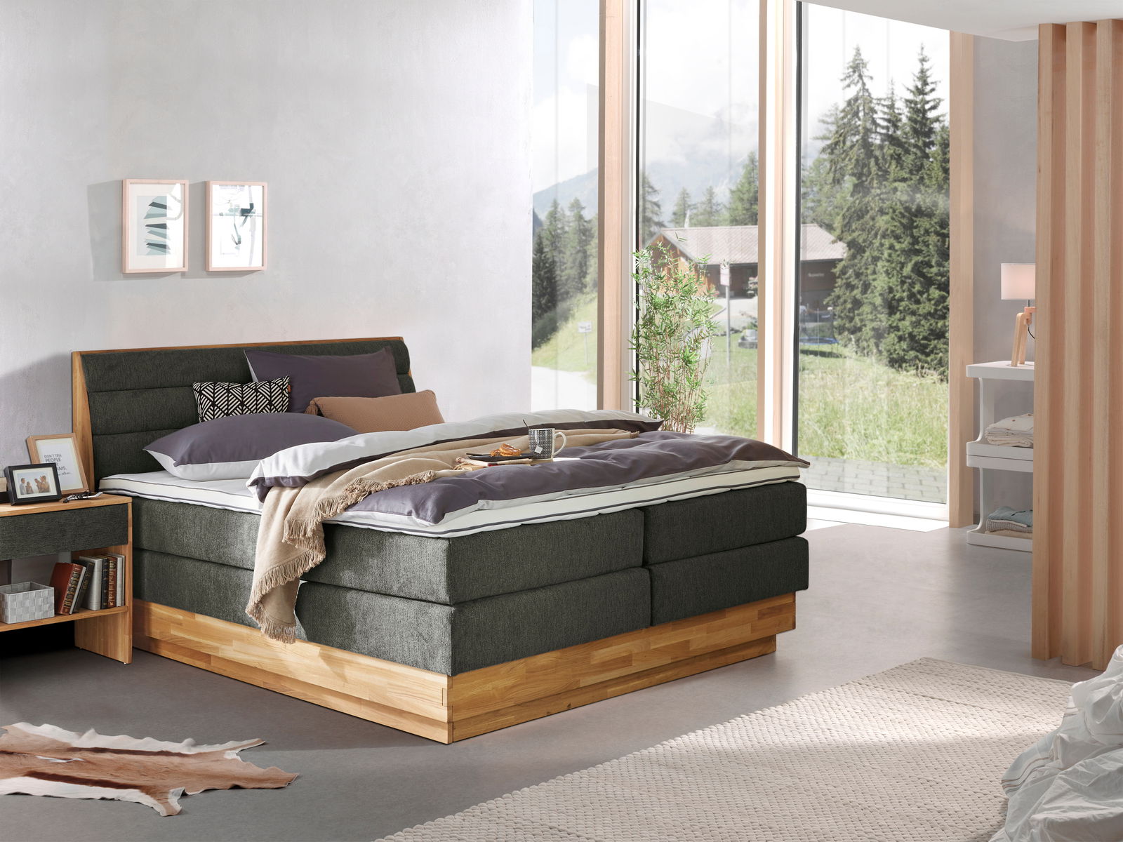 Z2 Boxspringbett MARISSA Modernes Boxspringbett in einem hellen Schlafzimmer mit großen Fenstern und Blick auf die Natur, seitliche Perspektive.