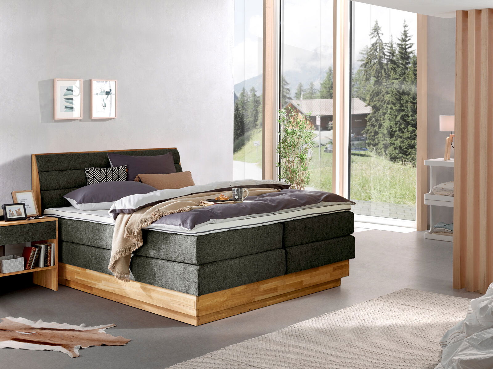 Z2 Boxspringbett MARISSA Modernes Boxspringbett in einem hellen Schlafzimmer mit großen Fenstern und Blick auf die Natur, seitliche Perspektive.