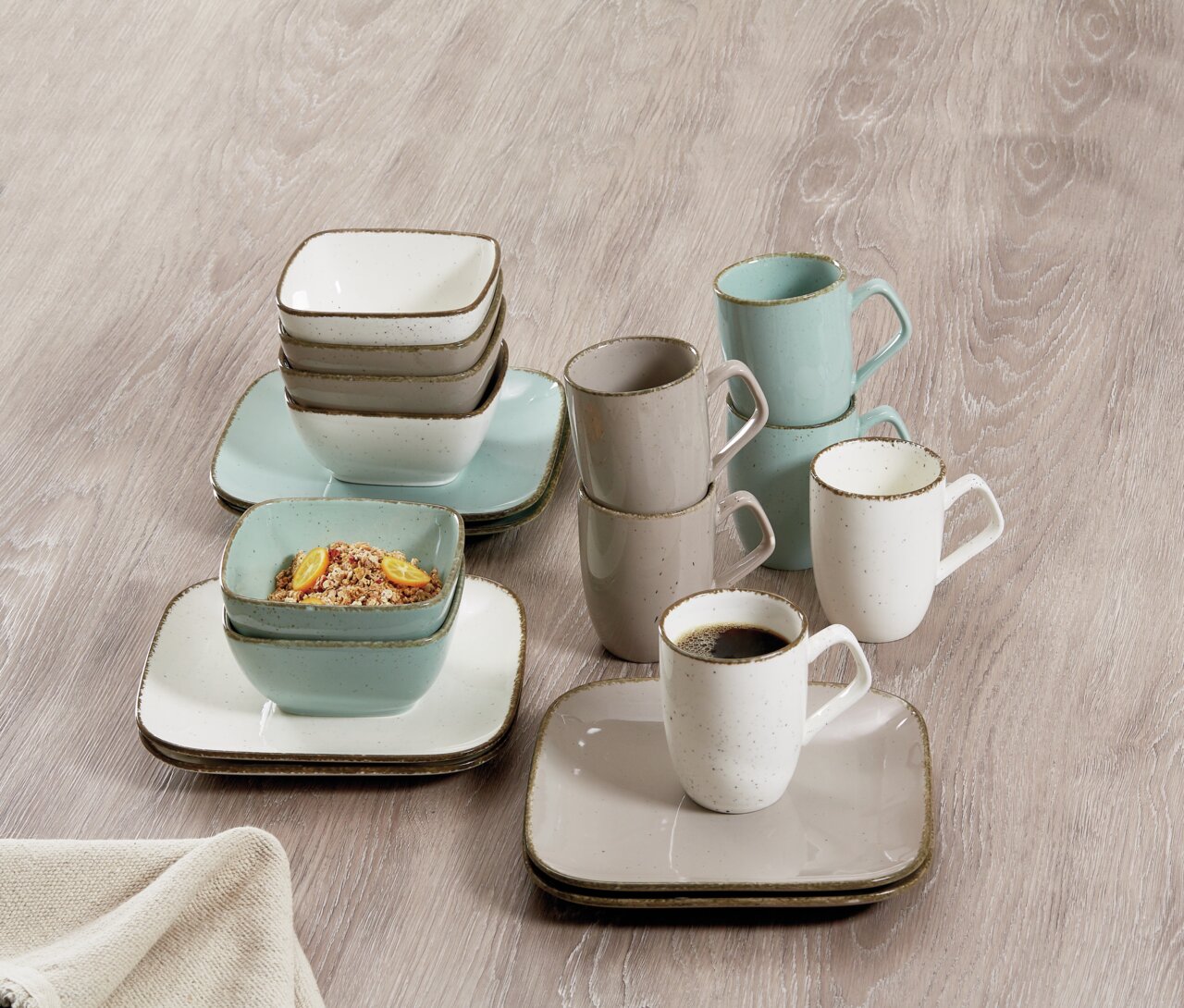 Koffieservies Casa, 18-delig, bestaande uit kopjes, schalen en borden in zachte pasteltinten, gefotografeerd van bovenaf op een houten ondergrond.