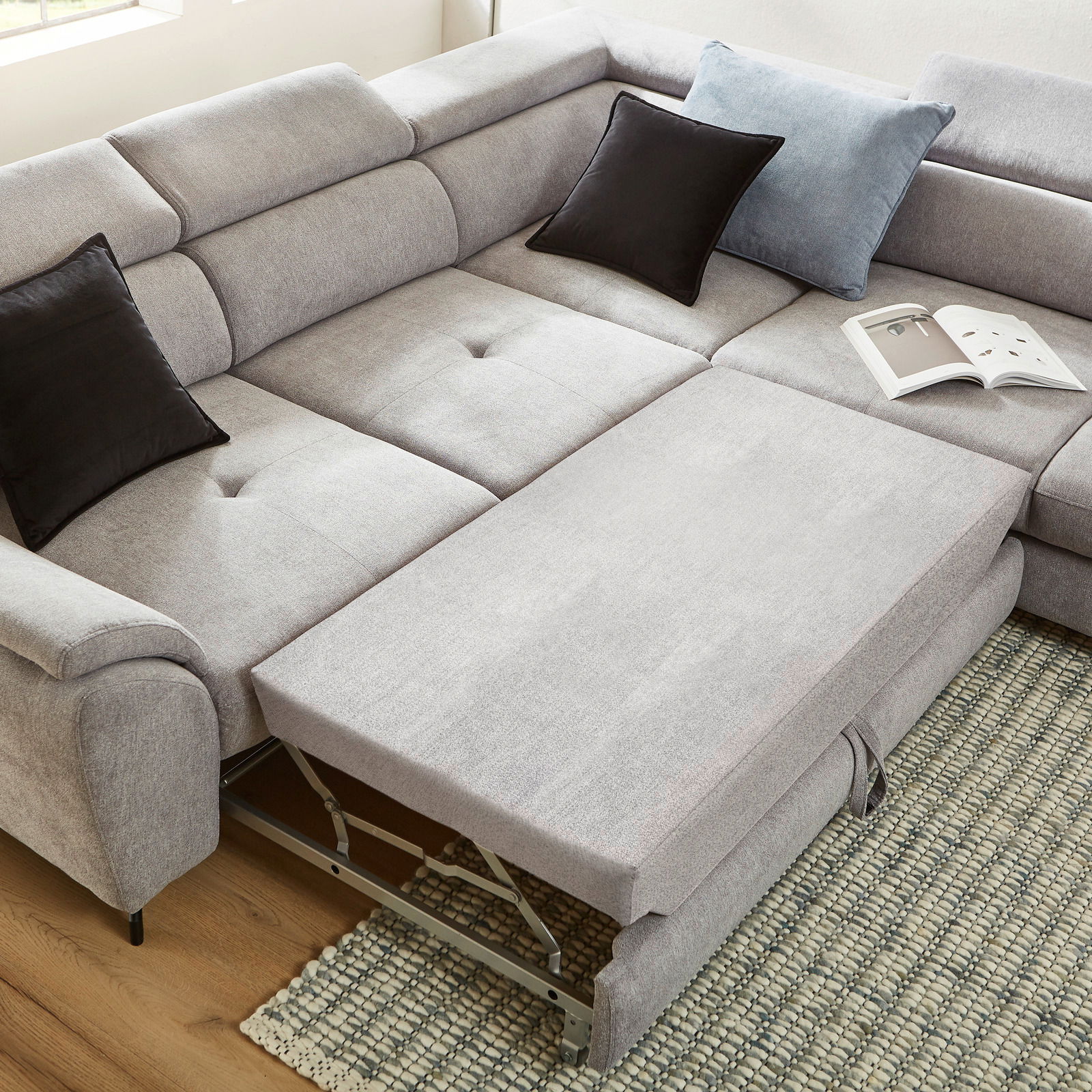 Ecksofa MAROLA in hellgrauem Stoff mit ausziehbarer Liegefläche, zwei schwarzen und einem blauen Kissen, aus der Vogelperspektive fotografiert.