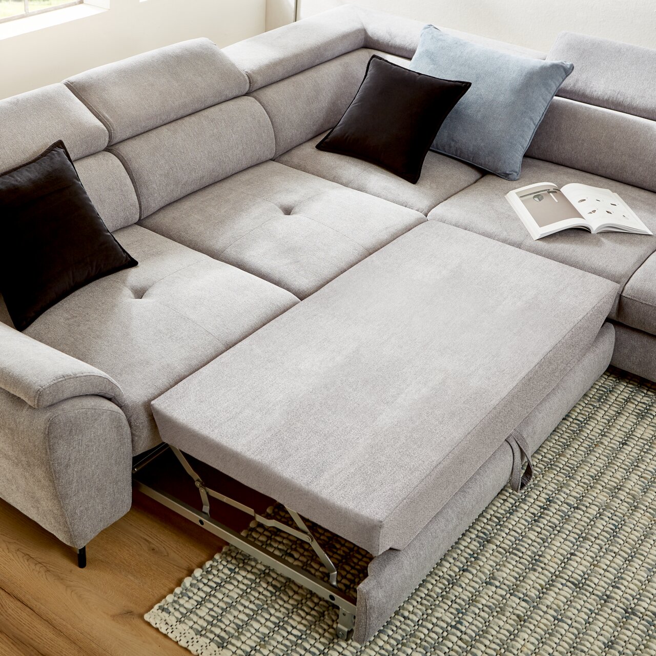 Ecksofa MAROLA in hellgrauem Stoff mit ausziehbarer Liegefläche, zwei schwarzen und einem blauen Kissen, aus der Vogelperspektive fotografiert.