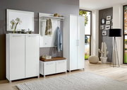 Modernes Garderoben-Set in Weiß, bestehend aus mehreren Schränken und einer Sitzbank, in einem hellen Raum mit großen Fenstern, seitliche Perspektive.