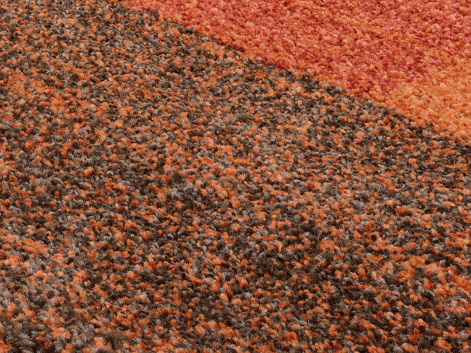 Nahaufnahme eines mehrfarbigen Teppichs mit orange und braunen Tönen, perspektivisch von oben fotografiert.