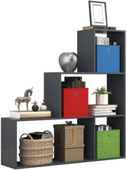 Modernes, dunkelgraues Stufenregal mit offenen Fächern, dekoriert mit Büchern, Pflanzen und farbigen Aufbewahrungsboxen (blau, rot, grün), in schräger Frontansicht freigestellt auf weißem Hintergrund.