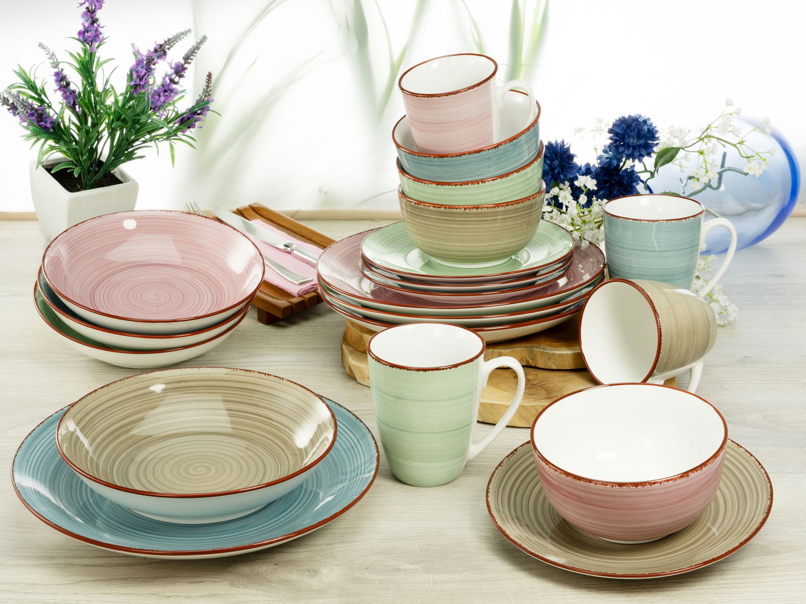 Creatable Kombiservice 20-tlg. SAMBA Kombiservice Samba 20-tlg. in verschiedenen Pastellfarben, bestehend aus Tellern, Schalen und Tassen, auf einem Tisch arrangiert, mit Blumen im Hintergrund, aus der Vogelperspektive fotografiert.