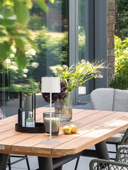 Moderne Akku-Tischleuchte SUN auf einem Holztisch im Freien, umgeben von Pflanzen und Dekorationen, seitliche Perspektive.