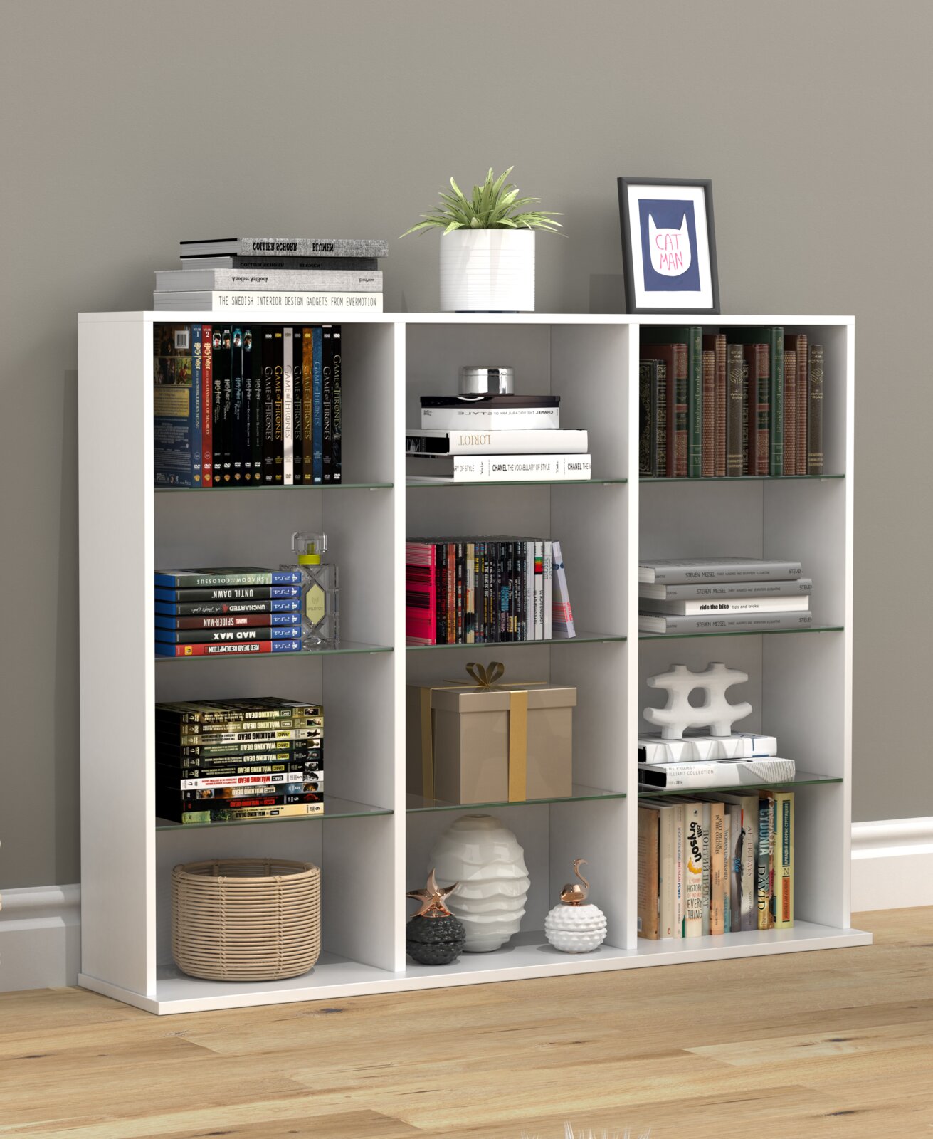 Weißes, modernes Regal mit neun Fächern und Glasböden, dekoriert mit Büchern, Pflanze, Bilderrahmen und Dekoobjekten; frontale Ansicht auf grauer Wand und Holzboden.