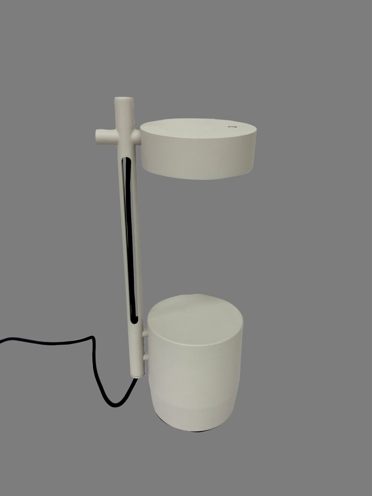 Weiße, minimalistische Tischleuchte mit zylindrischem Fuß und rundem Lampenkopf an vertikalem Stab, mit schwarzem Kabel, freigestellt auf grauem Hintergrund, Seitenansicht.