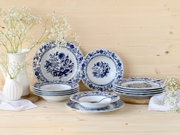 Blau-weißes Porzellan-Geschirrset mit floralem Dekor (Teller und Schalen) auf hellem Holztisch, dekoriert mit weißen Blumen und Besteck, aufgenommen in leicht erhöhter Frontalansicht.