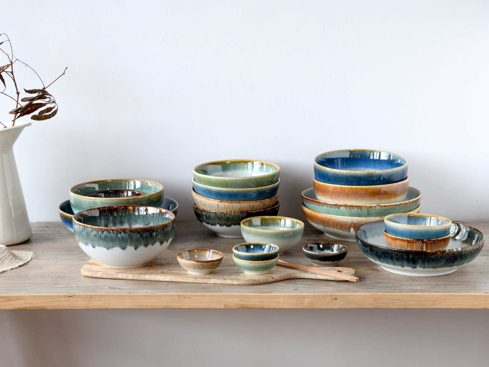 Creatable Bowl Set 12-tlg CASCADE Rustikales Keramik-Schüssel- und Schalen-Set in Blau-, Grün- und Sandtönen mit reaktiver Glasur, gestapelt auf einem Holztisch vor hellem Hintergrund, Perspektive: frontale Ansicht auf Augenhöhe.