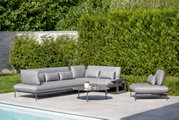Gartenlounge-Set mit grauem Loungesofa, Loungesessel und rundem Beistelltisch, umgeben von grüner Hecke, aus der Perspektive eines Betrachters am Pool.