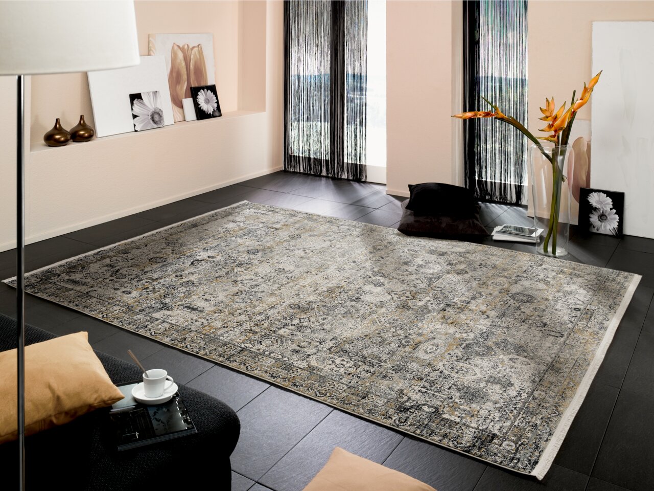 Designer Teppich in einem modernen Wohnzimmer, von schräg oben fotografiert, mit einem floralen Muster in Grau- und Beigetönen auf dunklem Boden.