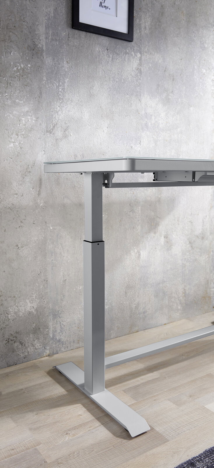 Seitliche Ansicht eines höhenverstellbaren E-Schreibtischs mit modernem Design und Metallgestell vor einer Betonwand.